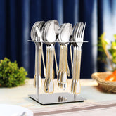 Gold-accented stainless cutlery displayed in upright stand on dining table with elegant curtain background.